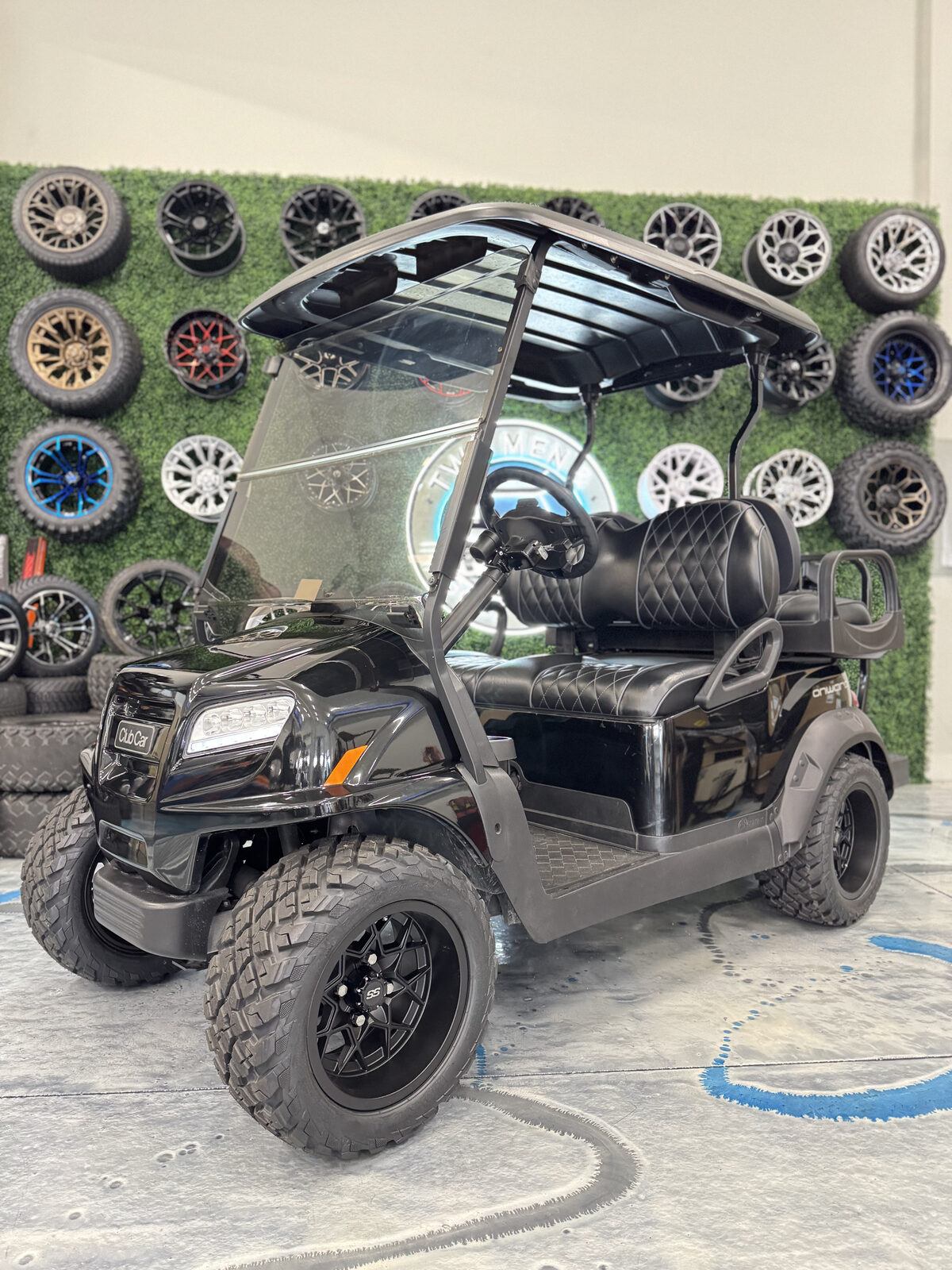 All-black Club Car Onward in front of custom wheel display wall