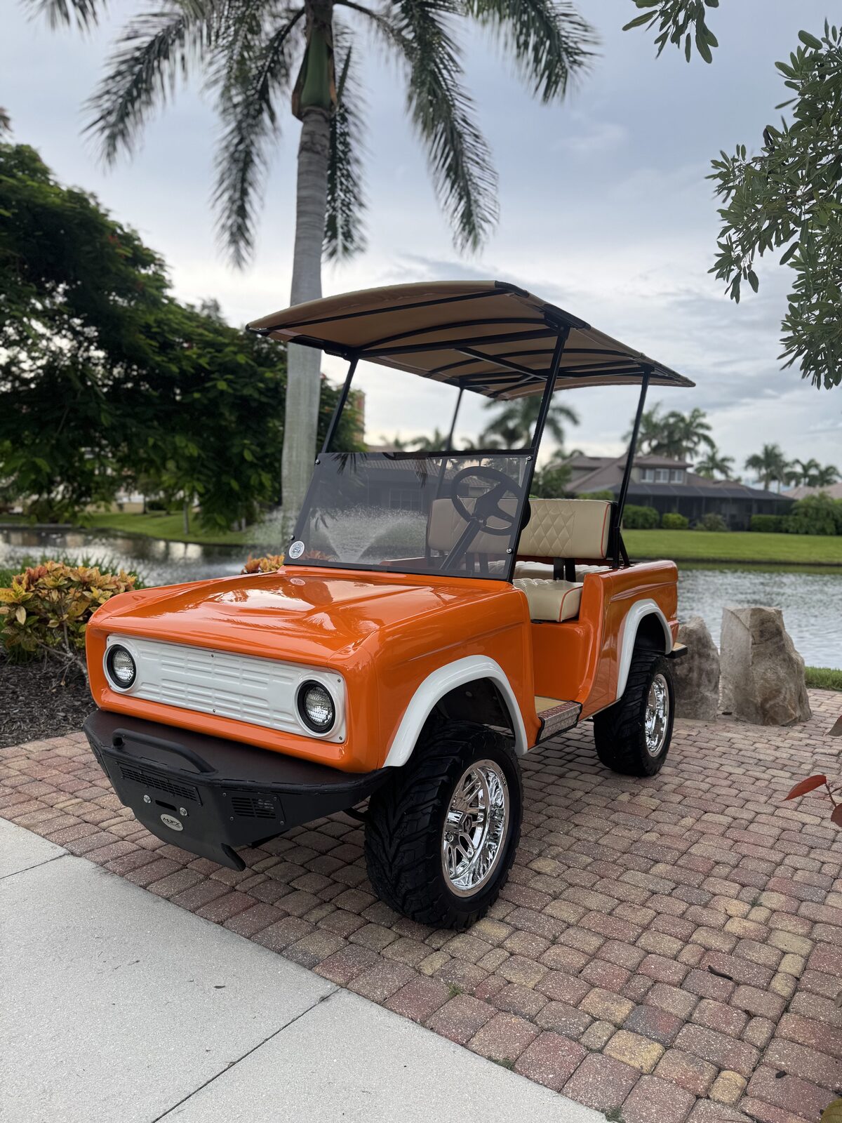 Orange and white classic Bronco-style golf cart by a Cape Coral lake at sunset